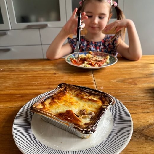 Lasaña de HoySeCome en su bandeja, con una nena comiendo en la mesa